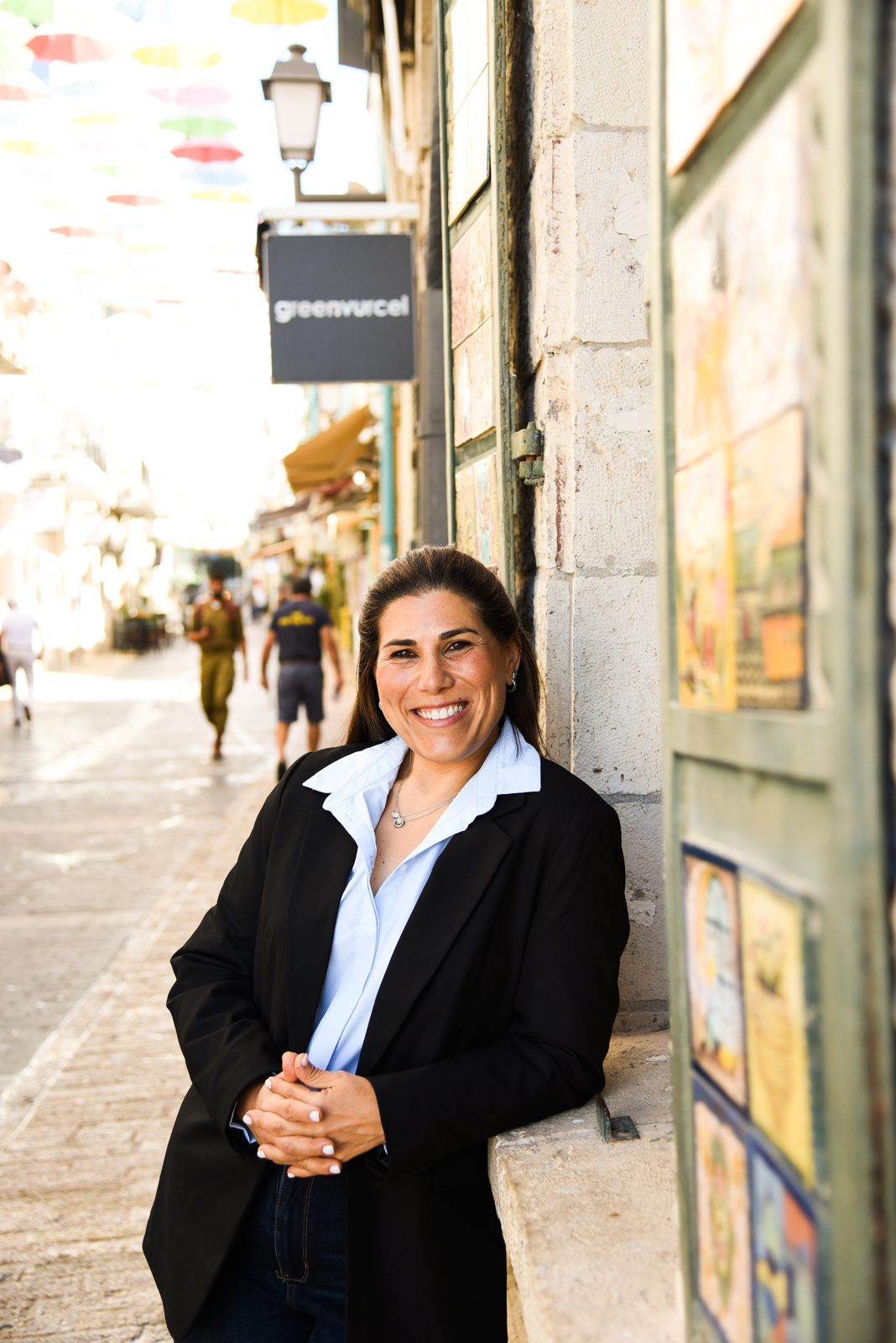 Michal Kaye smiling, leaning on a stone wall on a Jerusalem street